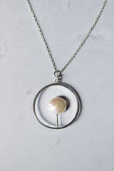 An open silver circle pendant with a Reiki imbued 10 mm white coin pearl attached to the inside hangs on a fine silver chain.