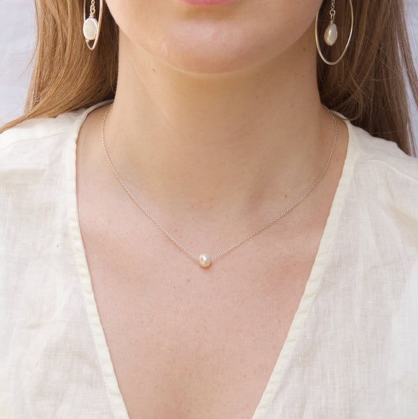 A round white pearl that is threaded onto a Reiki imbued silver chain which hangs delicately at the hollow of the neck. .