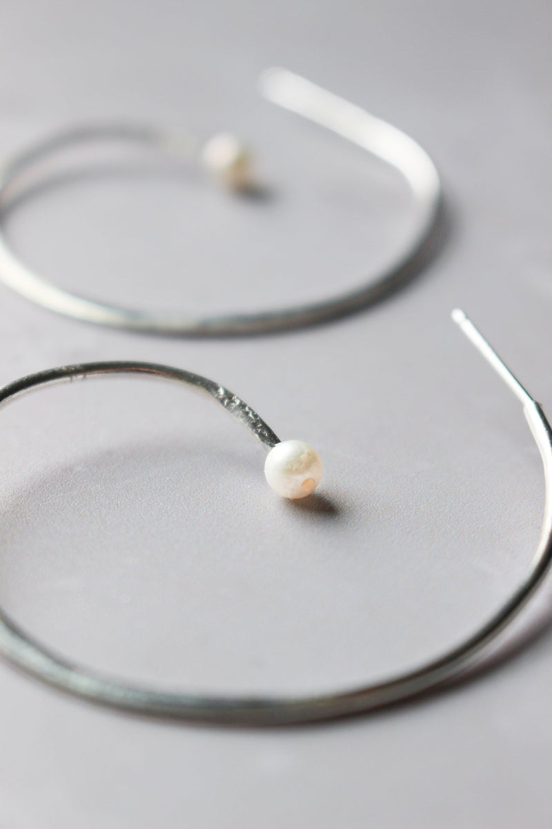 A pair of silver reiki imbued spiral hoop earrings with a small consciously sourced white pearl at the end tip of the spiral.