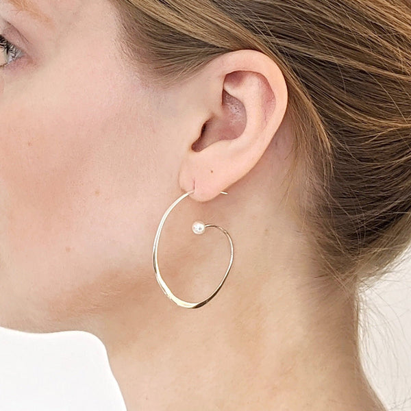 Model shows a silver reiki imbued medium size spiral hoop earring with a small consciously sourced white pearl at the end.