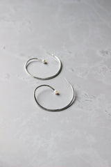 A pair of silver reiki imbued spiral hoop earrings with a small consciously sourced white pearl at the end tip of the spiral.