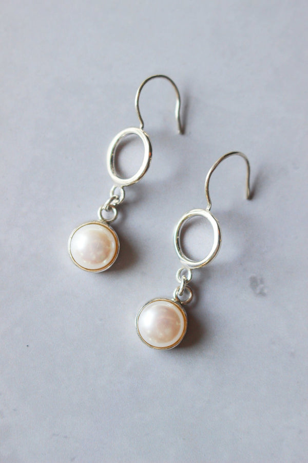 soft round silver ring  is attached to a shepherd hook. From it suspends an 8mm round white pearl set into a silver bezel.