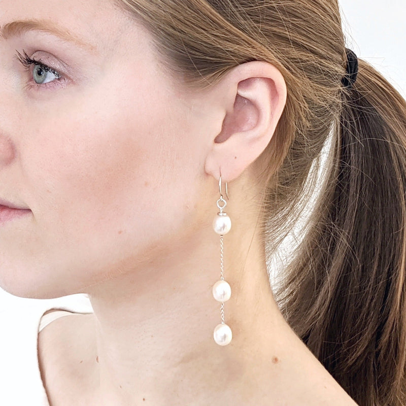 An earlobe shows three oval white pearls dangling almost to the shoulder on a silver chain, spaced to suggest acceleration.