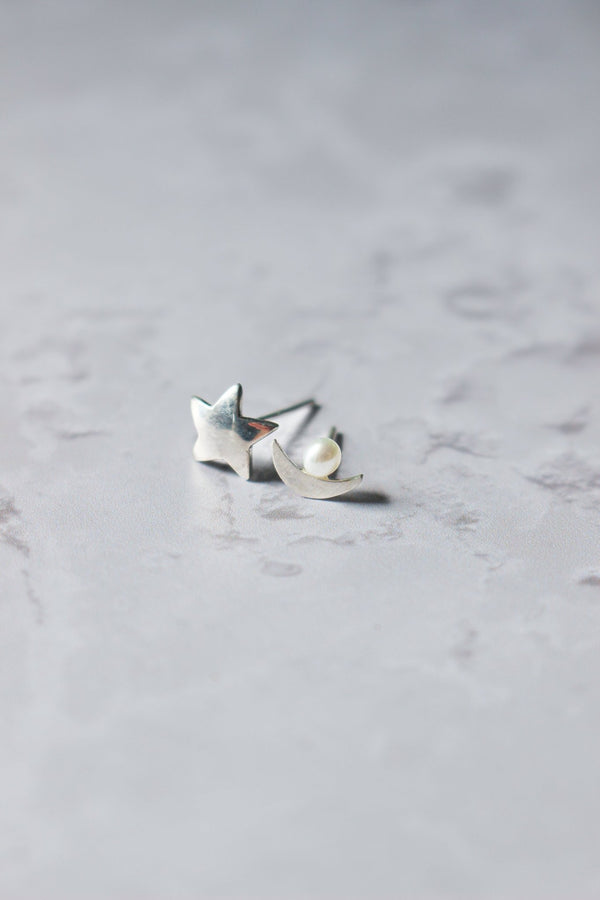 A silver star stud for one ear and a silver crescent moon for the other that has a small white pearl in the centre of the arc