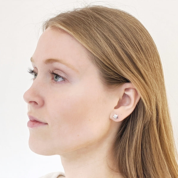 The side of a young woman’s face shows a delicate silver star stud earring imbued with Reiki energy.