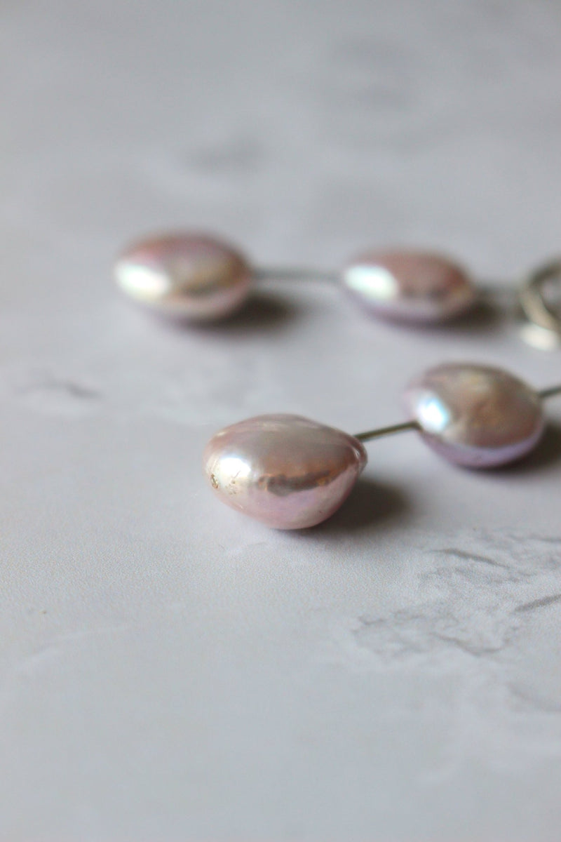 Two pink 10 mm coin pearls hang apart from one another on a single silver wire that drops from an open circle ear hook