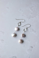 Two pink 10 mm coin pearls hang apart from one another on a single silver wire that drops from an open circle ear hook