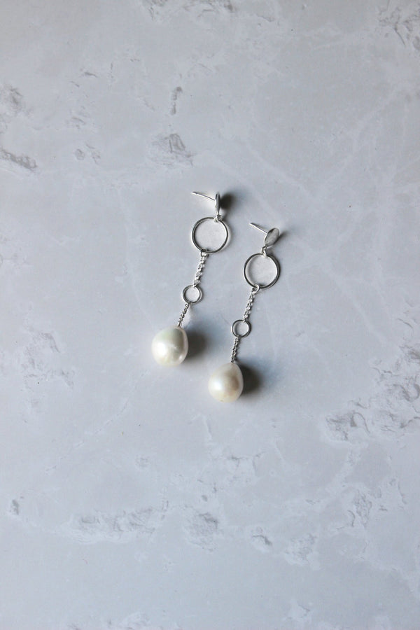 silver earrings feature a stud disc with a fine chain and teardrop shaped freshwater pearl at the end of the chain.