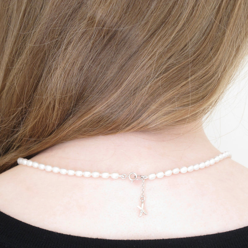 Model's nape shows the soft sterling silver X dangling just an inch from the closure of a handcrafted strand of white pearls
