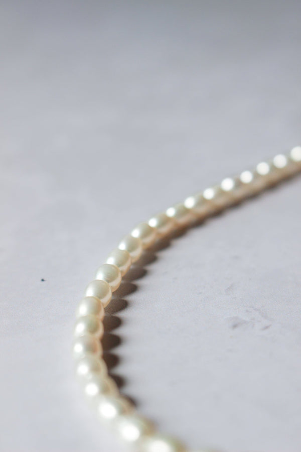 A closeup of a handcrafted necklace made with a strand of small oval freshwater white pearls