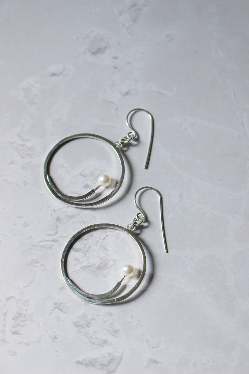 5 mm freshwater white pearl sits at the end of a silver arc that sits at the top inside a dangling handcrafted hoop earring