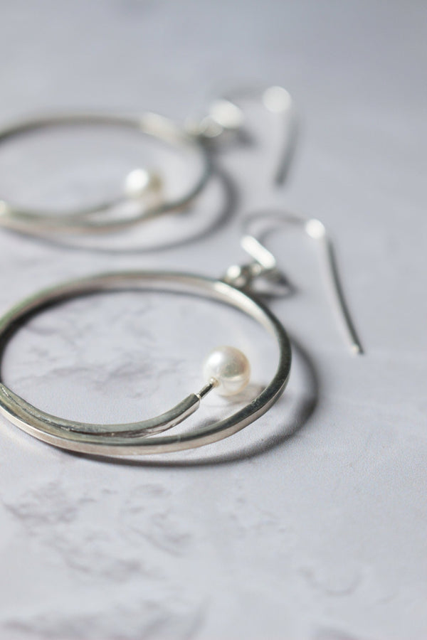 5 mm freshwater white pearl sits at the end of a silver arc that sits inside a large dangling handcrafted hoop earring
