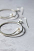 5 mm freshwater white pearl sits at the end of a silver arc that sits inside a large dangling handcrafted hoop earring