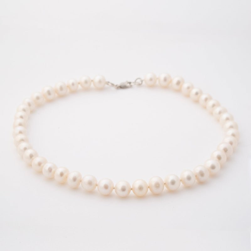 consciously sourced, handcrafted freshwater pearl strand imbued with Reiki laying in a perfect circle on a white surface.