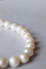 A close up of a strand of hand knotted necklace of white round pearls.