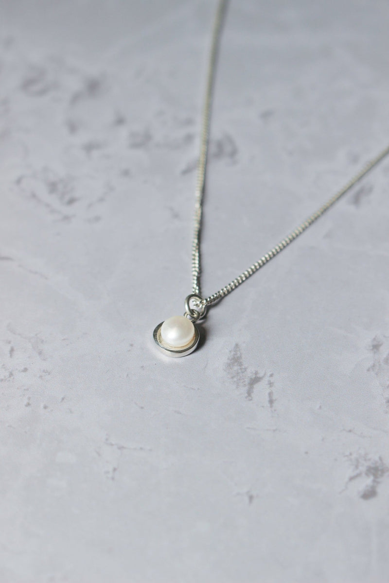 A round freshwater pearl sits in a handcrafted sterling silver halo that hangs from a chain.