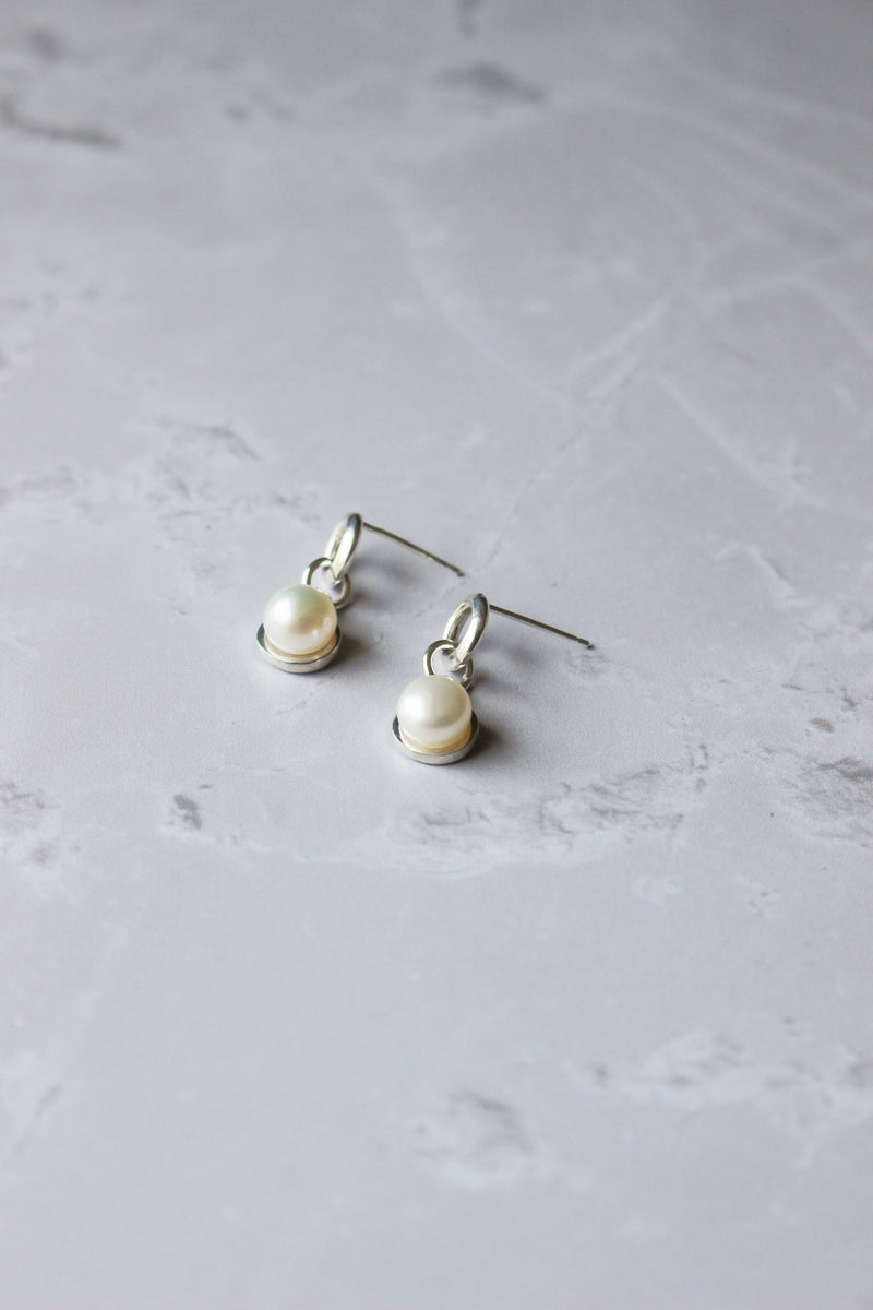 6 mm freshwater pearl earrings nestle in a halo of silver dangles from a soft modern round ring of silver with an ear posts